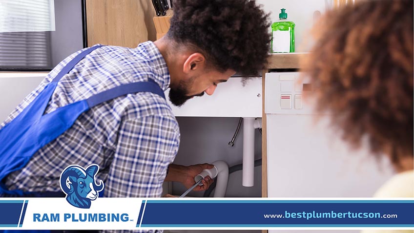 Woman Looking At Male Plumber Cleaning Clogged Pipes